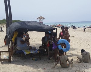La gente busca sombra como puede, ante el precio de alquilar una sombrilla de playa (Foto del autor)