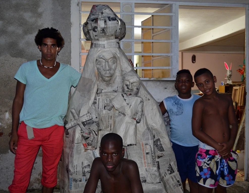 Luis Manuel Otero Alcántara, con niños de su comunidad y la escultura que usaría en su performance 'La Caridad nos une' 