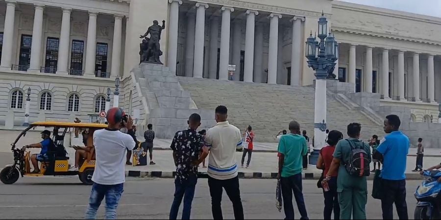 Un grupo de personas observa al manifestante, en lo más alto de la escalinata del Capitolio